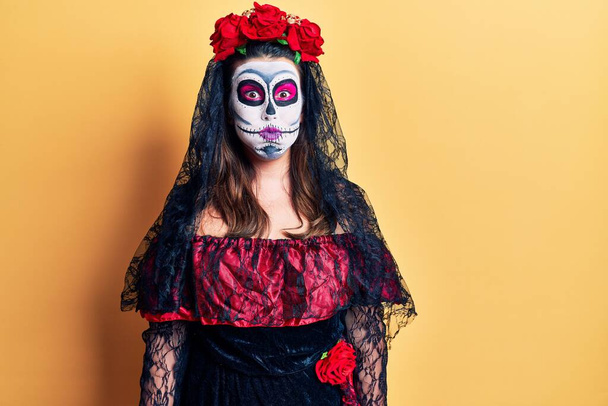 Young woman wearing day of the dead costume over yellow puffing cheeks with funny face. mouth inflated with air, crazy expression.  - Photo, Image