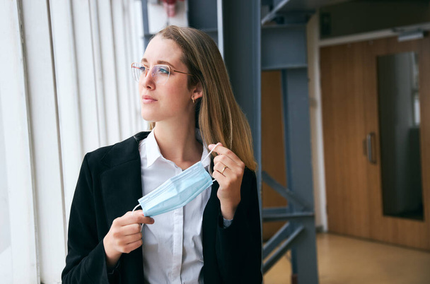 Молода бізнес-леді маскування стоячи в сучасному офісі під час здоров'я пандемії
 - Фото, зображення