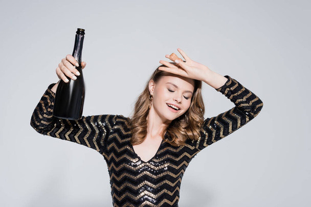 χαρούμενη γυναίκα κρατώντας μπουκάλι με σαμπάνια στο γκρι - Φωτογραφία, εικόνα