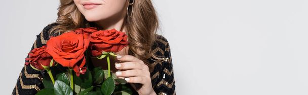 przycięty widok szczęśliwej młodej kobiety pachnącej bukiet czerwonych róż odizolowany na szarości - Zdjęcie, obraz