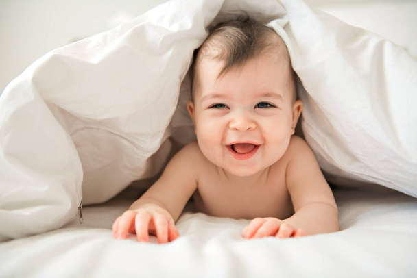 Cute baby girl sitting on the white bedding and smiling - Фото, зображення