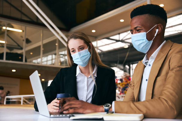 Pareja de negocios usando máscaras usando el ordenador portátil en el escritorio caliente en la oficina moderna durante la pandemia de la salud - Foto, imagen
