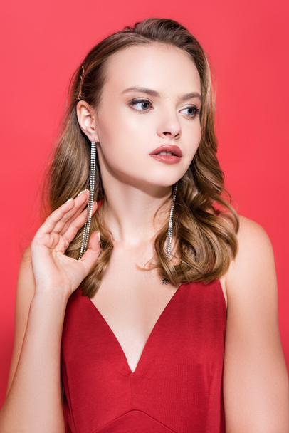 young woman in earrings looking away on red  - Фото, зображення