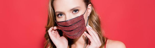 young woman wearing protective mask with rhinestones and looking at camera on red, banner - Photo, Image