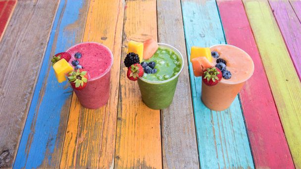 Barevné, chutné a zdravé ovocné koktejly na barevném dřevěném stole - Fotografie, Obrázek