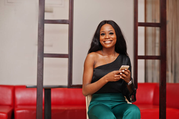 Beauty slim african american model wear on black blouse and green long legs pants posed at chinese cafe with mobile phone at hands. - Foto, Imagen
