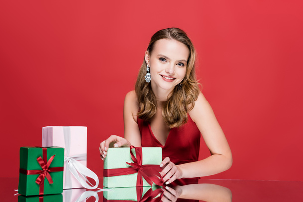 happy young woman smiling near christmas presents on red - Foto, Bild