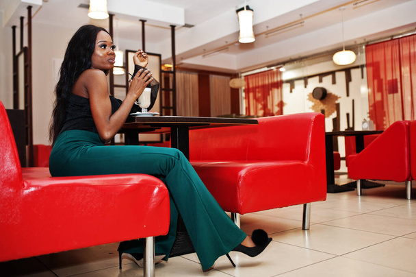 Beauty slim african american model wear on black blouse and green long legs pants drinking latte at chinese cafe. - Valokuva, kuva