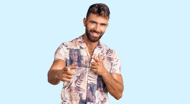 Jonge Spaanse man in zomerkleren die wijst naar camera 's met een vrolijk en grappig gezicht. goede energie en vibes.  - Foto, afbeelding