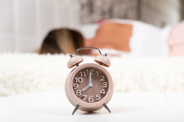 Close-up of an alarm clock on the table in the bedroom. Woman sleeping in the background, selective focus. The concept of starting a new day. - Valokuva, kuva