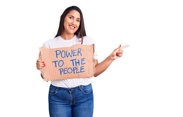 Young beautiful woman holding power to the people cardboard banner smiling happy pointing with hand and finger to the side  - Foto, Imagem