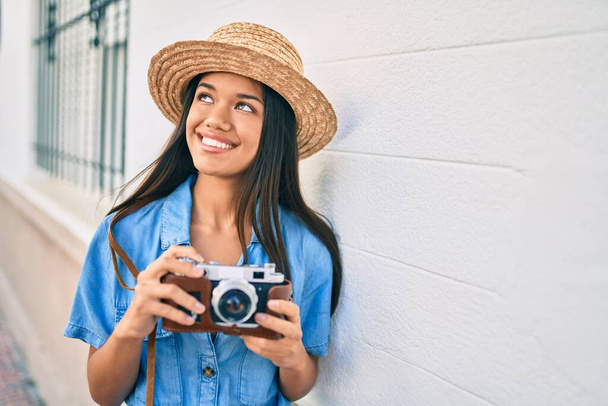 Молодая латинская туристка в отпуске улыбается счастливой с помощью винтажной камеры в городе. - Фото, изображение