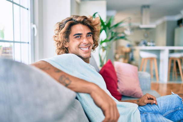 Young hispanic man smiling happy sitting on the sofa at home - Fotoğraf, Görsel
