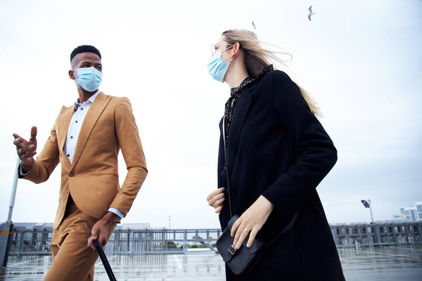 Деловая пара носит маски за пределами аэропорта для деловой поездки с багажом во время пандемии здоровья - Фото, изображение