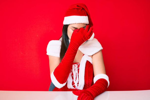 Giovane donna caucasica che indossa il costume di Babbo Natale stanco sfregamento naso e occhi sensazione di stanchezza e mal di testa. concetto di stress e frustrazione.  - Foto, immagini