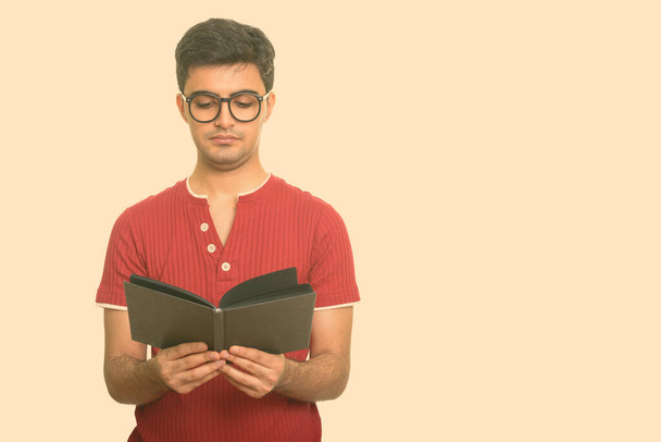 Portrait of young handsome Persian man reading book with eyeglasses - Foto, immagini