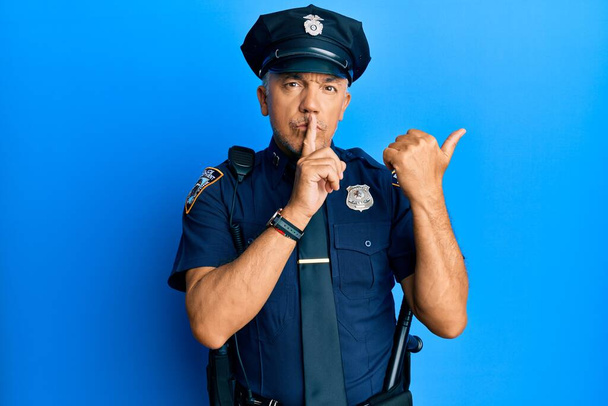 Pohledný dospělý muž středního věku v policejní uniformě žádá, aby byl zticha s prstem na rtech a ukazoval rukou na stranu. mlčení a tajný koncept.  - Fotografie, Obrázek