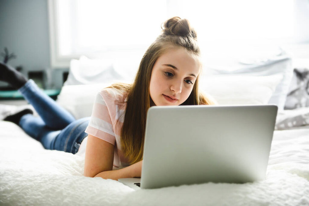 A Young smiling teen girl on bed with laptop - Фото, изображение
