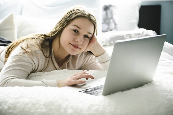 A Young smiling teen girl on bed with laptop - 写真・画像
