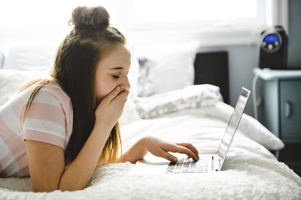Egy fiatal mosolygós tini lány az ágyban laptoppal - Fotó, kép