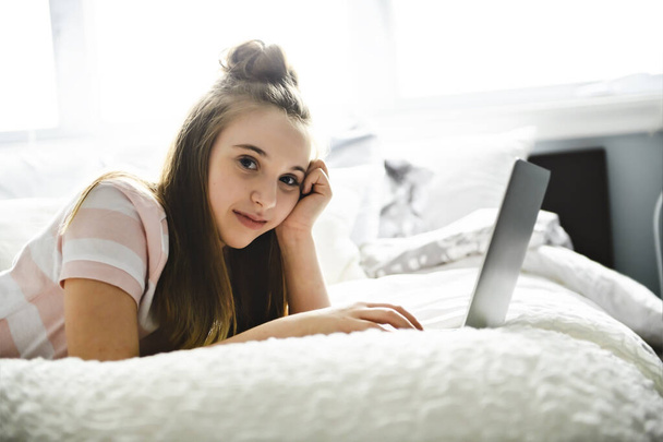 A Young smiling teen girl on bed with laptop - Fotografie, Obrázek