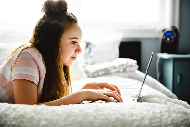 A Young smiling teen girl on bed with laptop - Foto, afbeelding