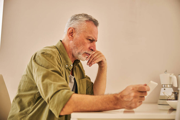 Concerned aging man checking his tablet and looking serious - Φωτογραφία, εικόνα
