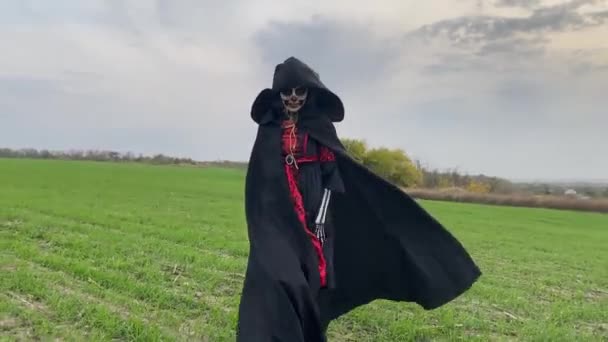 Jovem mulher caminha através do campo no traje de Halloween da morte com esqueleto pintado em seu corpo contra o céu de fundo. Conceito de Halloween. Maquiagem do crânio açúcar. - Filmagem, Vídeo