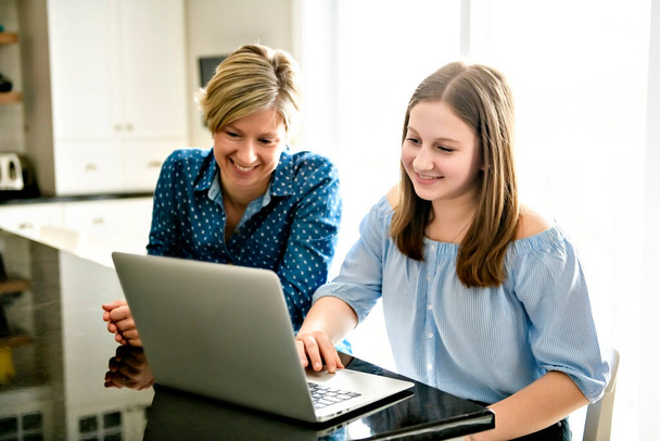 A mother using a laptop in kitchen with teenager - Foto, Imagen