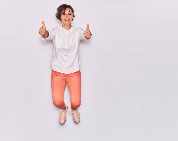 Young beautiful woman wearing casual clothes smiling happy. Jumping with smile on face doig ok sign with thumbs up over isolated white background. - Photo, Image
