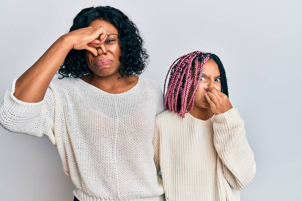 Όμορφη Αφροαμερικανή μητέρα και κόρη που φορούν καθημερινά ρούχα και αγκαλιάζονται μυρίζοντας κάτι βρωμερό και αηδιαστικό, ανυπόφορη μυρωδιά, κρατώντας την αναπνοή με δάχτυλα στη μύτη. άσχημη μυρωδιά  - Φωτογραφία, εικόνα
