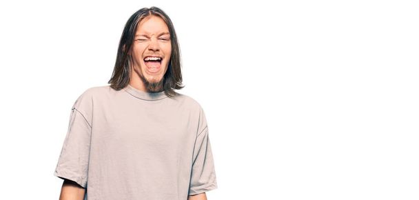 Handsome caucasian man with long hair wearing casual clothes winking looking at the camera with sexy expression, cheerful and happy face.  - Fotó, kép