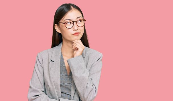 若い中国人女性を身に着けているビジネス服深刻な顔を考えて質問について手であご,混乱のアイデアについて思慮深い  - 写真・画像