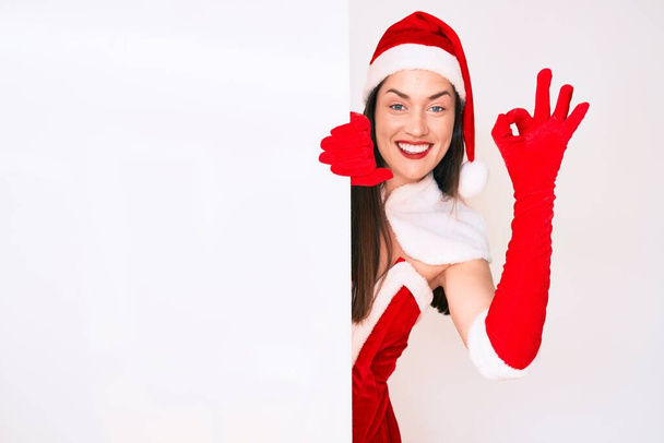 Noel Baba kostümü giyen genç bir kadın elinde boş pankartla tamam işareti yapıyor, gülümseyerek mükemmel bir sembol oluşturuyor.  - Fotoğraf, Görsel