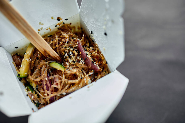 Lekkere Udon noedels pasta met tempuru, garnalen wok in doos levering en houten stokjes, Japans kruidig eten, Doos met Thais eten, concept van fast food levering. - Foto, afbeelding