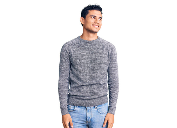 Hombre joven guapo hispano con suéter casual mirando hacia otro lado con sonrisa en la cara, expresión natural. riendo confiado.  - Foto, imagen