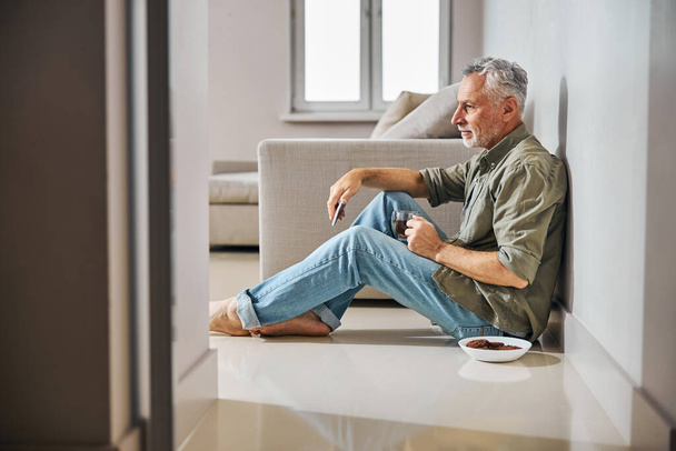 Grey-haired gentleman having tea with cookies on the floor - Fotografie, Obrázek