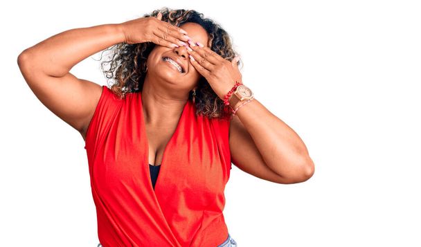 Young african american plus size woman wearing casual style with sleeveless shirt covering eyes with hands smiling cheerful and funny. blind concept.  - Foto, Imagem