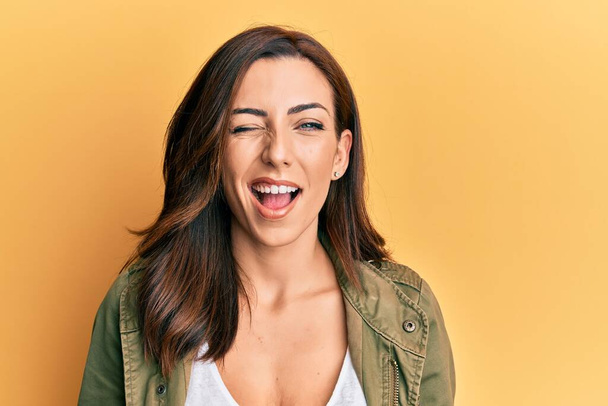 Young brunette woman wearing casual clothes over yellow background winking looking at the camera with sexy expression, cheerful and happy face.  - Photo, Image