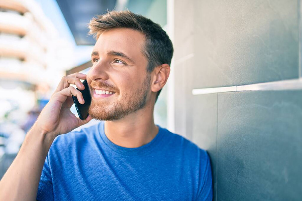 Nuori valkoihoinen mies hymyilee onnellinen puhuminen älypuhelimella kaupungin. - Valokuva, kuva