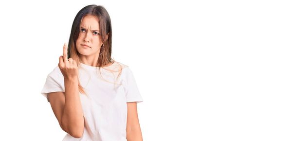 Beautiful caucasian woman wearing casual white tshirt showing middle finger, impolite and rude fuck off expression  - 写真・画像
