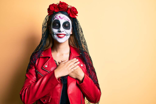 Woman wearing day of the dead costume over yellow smiling with hands on chest with closed eyes and grateful gesture on face. health concept.  - Foto, Imagen