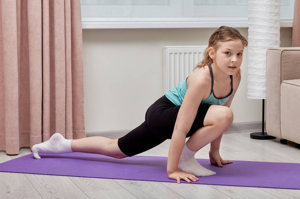 A girl performs sports exercises at home on a sports Mat. Looks at the camera. - Фото, зображення