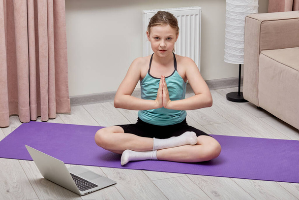 A beautiful cute girl does yoga at home using a laptop and a training lesson. - Photo, Image