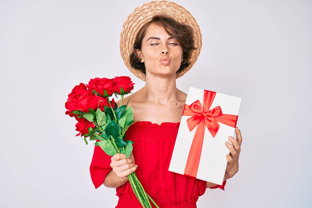 Mujer hispana joven sosteniendo regalo y ramo de flores para aniversario mirando a la cámara soplando un beso siendo encantadora y sexy. expresión de amor.  - Foto, Imagen