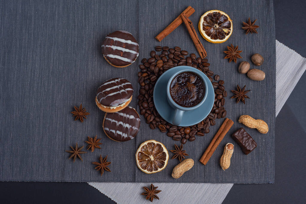 A cup of espresso is decorated with anise stars, cinnamon, sweets, dried lemons, acorns, peanuts in a beautiful dish. - Foto, Imagem