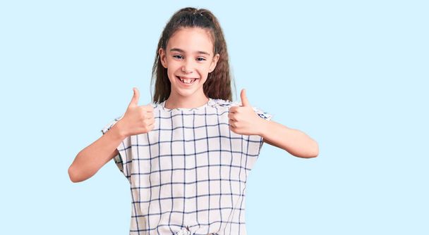 Cute hispanic child girl wearing casual clothes success sign doing positive gesture with hand, thumbs up smiling and happy. cheerful expression and winner gesture.  - Фото, зображення