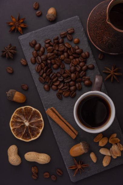 A cup of espresso is decorated with anise stars, cinnamon, sweets, dried lemons, acorns, peanuts in a beautiful dish. - Photo, Image