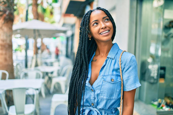 Νεαρή Αφρικάνα Αμερικανίδα χαμογελά χαρούμενη περπατώντας στην πόλη. - Φωτογραφία, εικόνα