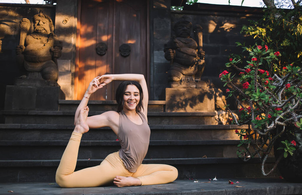 Ganzkörper positiver schlanker Frau in Sportbekleidung, die Yogaübungen macht, während sie auf der Treppe im Park auf Bali Meerjungfrauen posiert - Foto, Bild